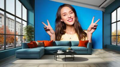 gesture and people concept - smiling young woman or teenage girl showing peace hand sign over bright blue background Wall mural