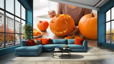 halloween, decoration and holidays concept - close up of woman with spoon carving pumpkin flesh and making or jack-o-lantern at home Wall mural