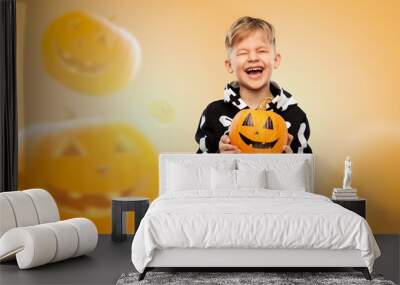 halloween, holiday and childhood concept - happy laughing boy in black costume with skeleton bones holding jack-o-lantern over pumpkins on background Wall mural