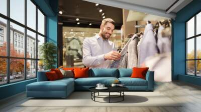 happy young man choosing clothes in clothing store Wall mural