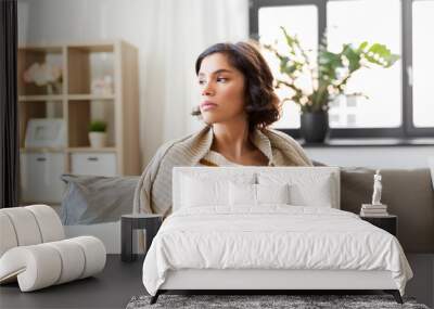 health, cold and people concept - sad sick young woman in blanket sitting on sofa and drinking hot tea at home Wall mural