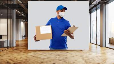 health, safety and pandemic concept - happy indian delivery man wearing face protective medical mask for protection from virus disease with parcel box and clipboard in uniform over grey background Wall mural