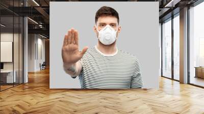 health protection, safety and pandemic concept - young man in protective mask or respirator with valve making stop gesture over grey background Wall mural