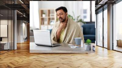 healthcare, technology and people concept - sick indian man in blanket with sore throat having video call on laptop computer at home Wall mural