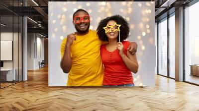 holidays, photo booth and people concept - happy african american couple with party props hugging over festive lights background Wall mural