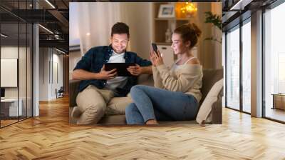 leisure, technology and internet addiction concept - happy couple with tablet computer and smartphone at home in evening Wall mural