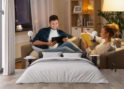 leisure and people concept - happy couple with tablet computer and book at home in evening Wall mural