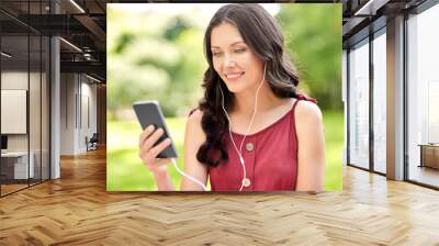 leisure and people concept - portrait of happy smiling woman with smartphone and earphones listening to music at summer park Wall mural