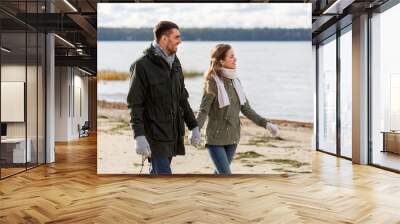 love, relationship and people concept - smiling couple walking along autumn beach and holding hands Wall mural