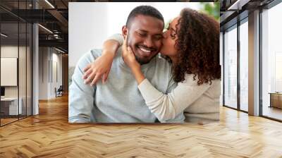 love, valentines day and relationships concept - happy african american couple sitting on sofa at home and kissing Wall mural