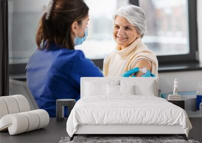 medicine, health and vaccination concept - doctor or nurse applying medical patch to vaccinated senior woman at hospital Wall mural