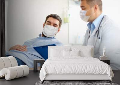 medicine, healthcare and pandemic concept - doctor wearing face protective medical mask for protection from virus disease with clipboard and young male patient at medical exam at hospital Wall mural