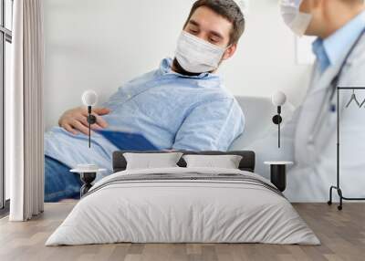 medicine, healthcare and pandemic concept - doctor wearing face protective medical mask for protection from virus disease with clipboard and young male patient at medical exam at hospital Wall mural