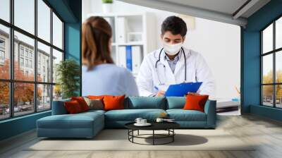 medicine, healthcare and pandemic concept - indian doctor wearing protective medical mask for protection from virus with clipboard and patient at hospital Wall mural