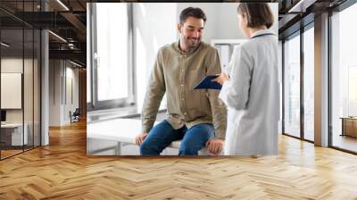 medicine, healthcare and people concept - female doctor with clipboard and happy smiling man patient meeting at hospital Wall mural