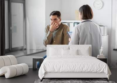 medicine, healthcare and people concept - female doctor with clipboard and man patient touching his nose at hospital Wall mural