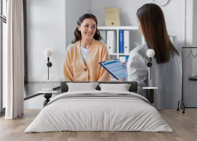 medicine, healthcare and people concept - female doctor with clipboard talking to smiling woman pati Wall mural