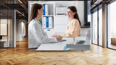 medicine, healthcare and people concept - female doctor with clipboard talking to smiling woman patient at hospital Wall mural