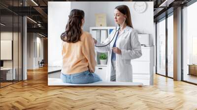 medicine, healthcare and people concept - female doctor with stethoscope listening to woman patient at hospital Wall mural