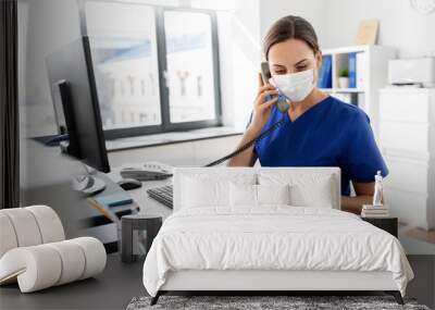 medicine, people and healthcare concept - female doctor or nurse wearing face protective medical mask for protection from virus disease with computer and clipboard calling on phone at hospital Wall mural