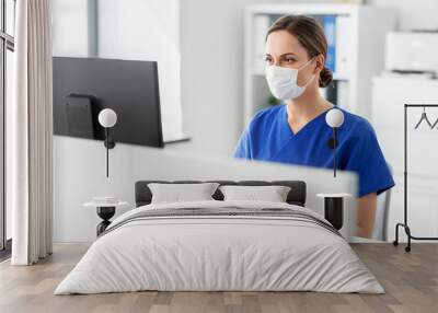 medicine, technology and healthcare concept - female doctor or nurse wearing face protective medical mask for protection from virus disease with computer working at hospital Wall mural