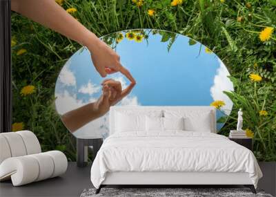 nature concept - hand touching sky reflection in round mirror on summer field Wall mural