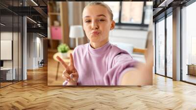 people, gesture and technology concept - happy smiling girl taking selfie at home, making duck face and showing peace sign Wall mural