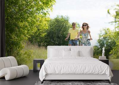 people, leisure and lifestyle concept - happy young couple riding bicycles along road in summer Wall mural