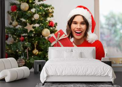 people, presents and holidays concept - happy smiling young woman in santa helper hat with red gift box over christmas tree on background Wall mural