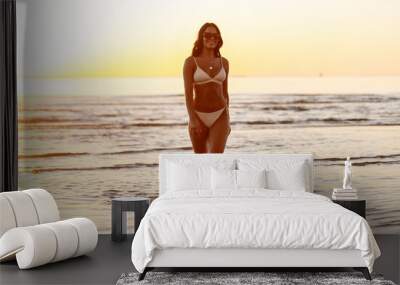 people, summer and leisure concept - happy smiling young woman in bikini swimsuit on beach over sunset Wall mural