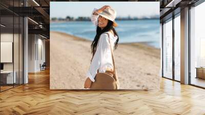 people, summer holidays and leisure concept - happy smiling woman in white shirt and straw hat with jute bag walking along beach Wall mural