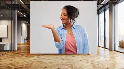 people and advertisement concept - happy african american young woman holding something imaginary on empty hand over pink background Wall mural