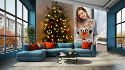 people and holidays concept - happy young woman wearing ugly sweater with reindeer pattern over home and christmas tree lights on background Wall mural