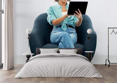 people and technology concept - portrait of smiling young woman in turquoise shirt and jeans with tablet pc computer sitting in modern armchair over grey background Wall mural