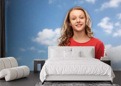 people concept - smiling teenage girl with long hair in red t-shirt over blue sky and clouds background Wall mural