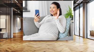 pregnancy, rest, people and expectation concept - happy smiling pregnant asian woman sitting on sofa at home having video call on smartphone Wall mural