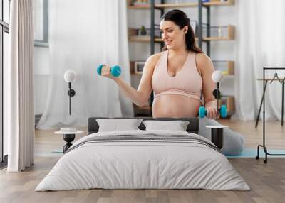 pregnancy, sport and fitness concept - happy pregnant woman with light dumbbells exercising at home Wall mural