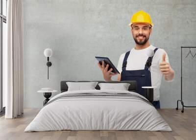 profession, construction and building concept - happy smiling male worker or builder in yellow helmet and overall with tablet pc computer showing thumbs up over grey concrete background Wall mural