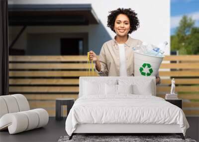 recycling, waste sorting and sustainability concept - smiling woman holding rubbish bin with plastic bottles and trash bag over living house background Wall mural