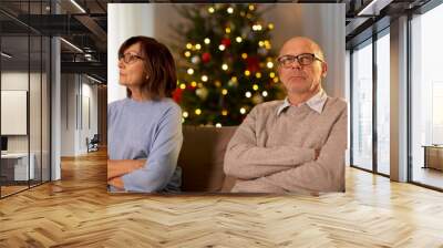 relationships difficulties, problem and people concept - unhappy senior couple sitting on sofa at home over christmas tree lights on background Wall mural