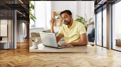 remote job, technology and people concept - bored or tired young indian man in glasses with laptop computer working at home office Wall mural