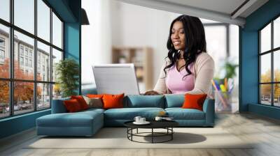 remote job, technology and people concept - happy smiling african american young woman with laptop computer working at home office Wall mural