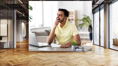 remote job, technology and people concept - young indian man with notebook and laptop computer at home office Wall mural