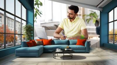 remote job, technology and people concept - young indian man with notebook and laptop computer at home office Wall mural