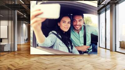 road trip, leisure, couple, technology and people concept - happy man and woman driving in car and taking selfie with smartphone Wall mural