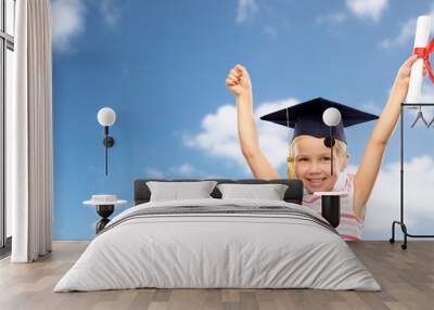 school, education and learning concept - happy little girl in bachelor hat or mortarboard with diploma celebrating success over blue sky and clouds background Wall mural