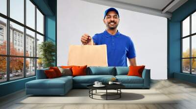 service and people concept - happy indian delivery man food in paper bag in blue uniform over grey background Wall mural