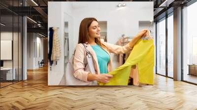 shopping, fashion, sale and people concept - happy young woman choosing dress in mall or clothing store Wall mural