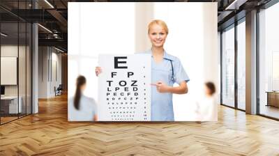 smiling female doctor or nurse with eye chart Wall mural