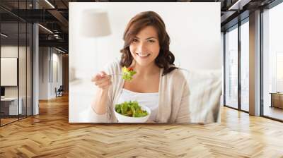 smiling young woman eating salad at home Wall mural